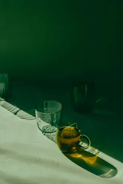 Three glasses with low light so they cast a long shadow. One of the glasses has a handle with tea in it, the others are empty.