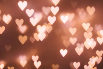 A reddy/brown image with light, bright love hearts randomly scatters with various levels of focus.