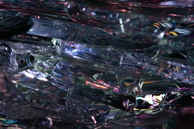 An abstract closeup of broken glass on a black background with pink and purple light reflections.